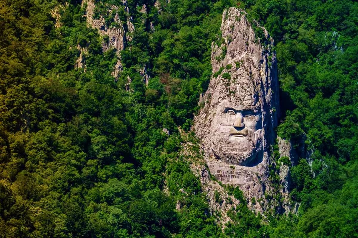 Decebalus Rex carved stone face monument on cliff surrounded by dense green forest in Danube Gorge, Serbia