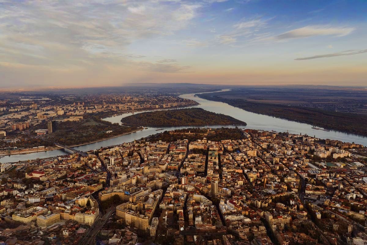 Aerial view of Zemun and Belgrade separated by the Danube River, with historic architecture and forested islands at sunset