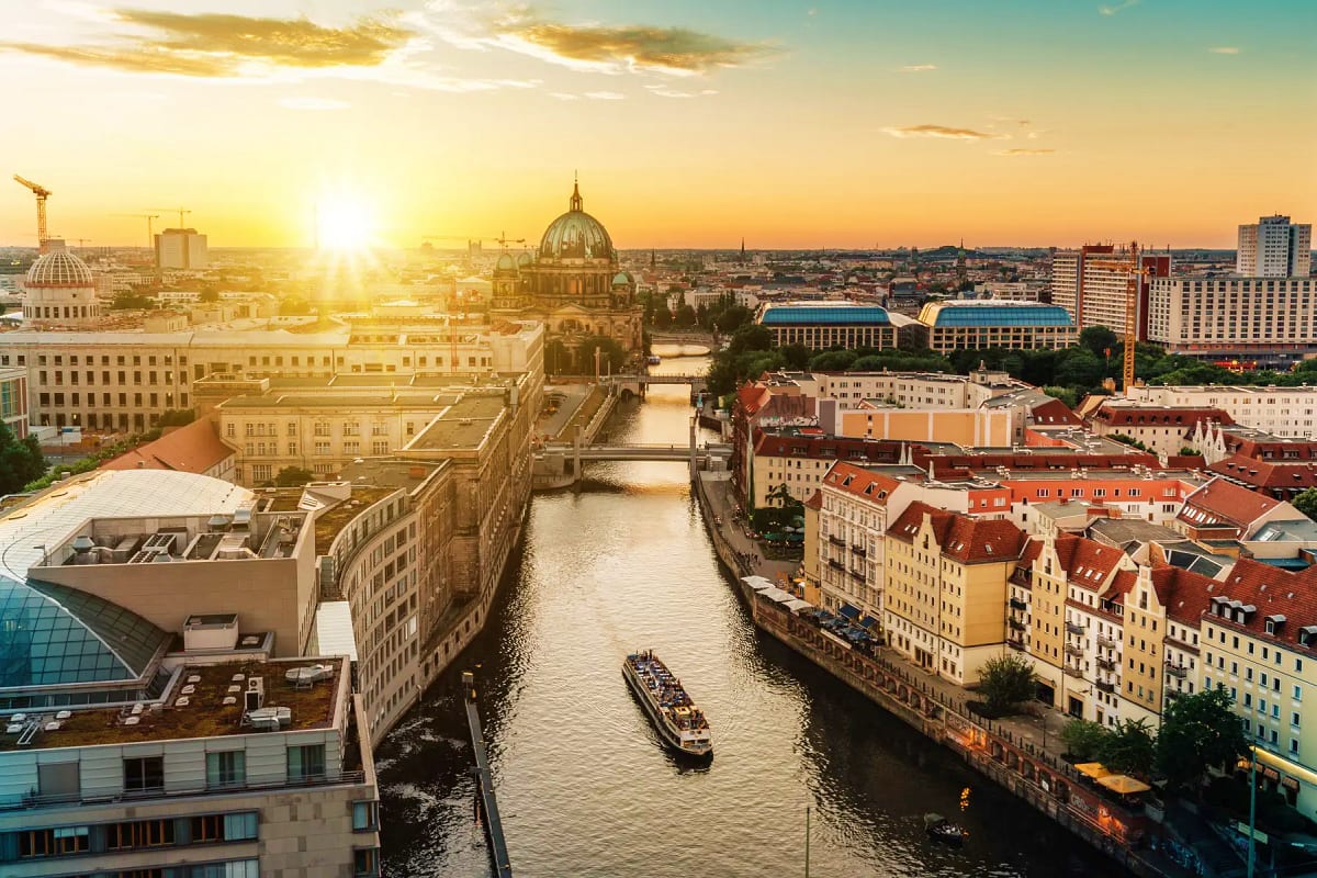 Sunset view of Berlin cityscape with Spree River, tour boat, Berlin Cathedral dome, and historic architecture along the water