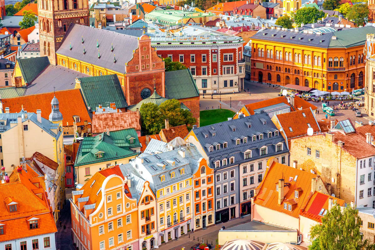 Aerial view of colorful historic buildings with orange and red roofs in a European old town square, featuring a brick cathedr