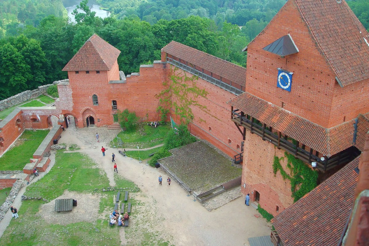 Aerial view of Trakai Castle with red brick towers, courtyard, and visitors exploring the medieval fortress surrounded by gre