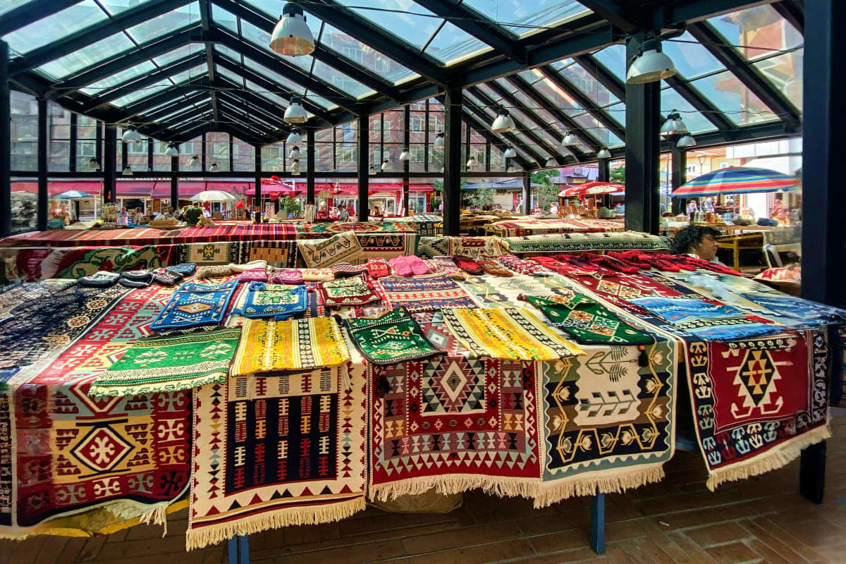 Traditional Albanian carpets with geometric patterns displayed under glass roof at outdoor market in Tirana