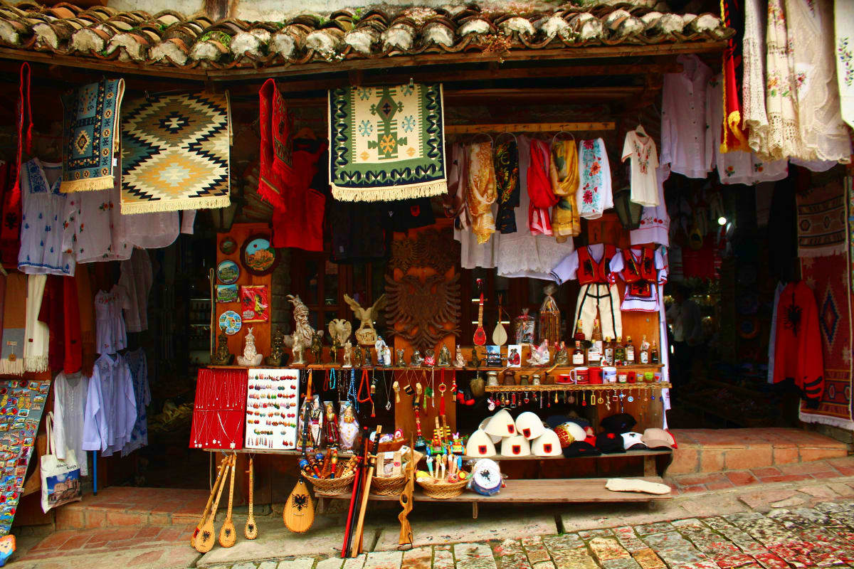 Traditional Albanian souvenir shop storefront displaying embroidered textiles, handmade crafts, red decorative items, and fol