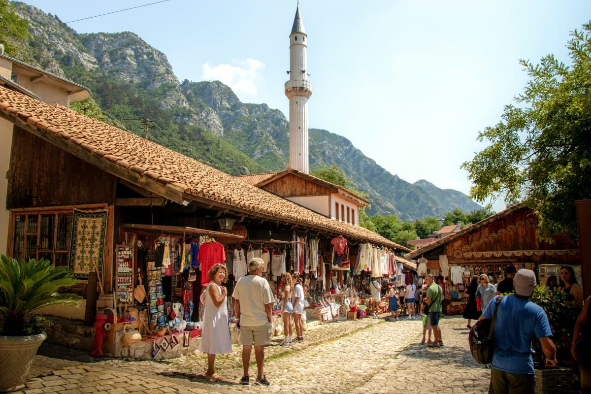 Bustling bazaar in Kotor Old Town with traditional shops, tourists browsing souvenirs, and a minaret visible against forested