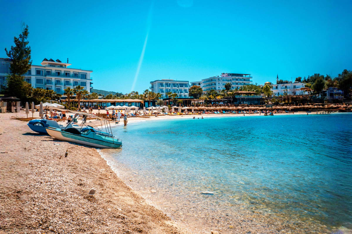 Blue fishing boats beached at a sandy Mediterranean cove with clear turquoise water, hotels and buildings on the shoreline un