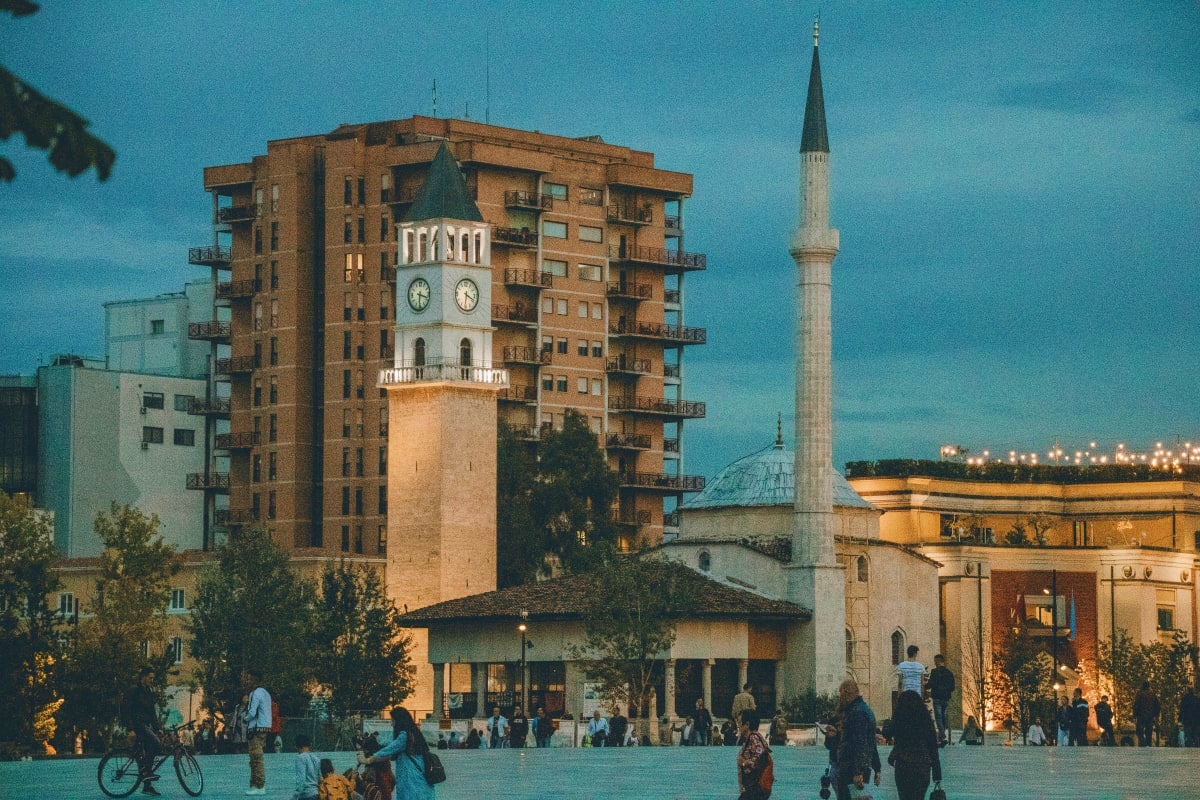 Clock tower and mosque with minaret in Skanderbeg Square, Tirana, Albania at dusk with locals and visitors