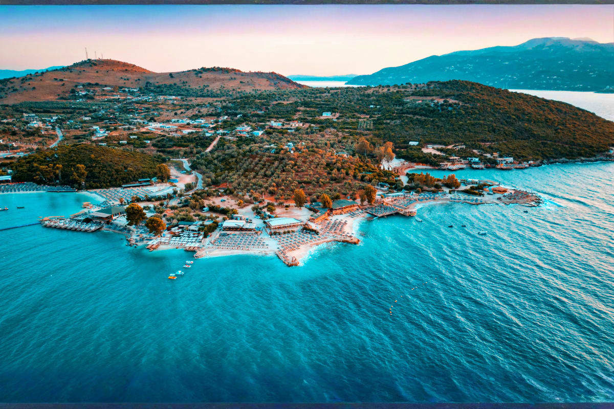 Aerial view of turquoise Adriatic Sea with coastal town, beaches, and forested hills in Albania