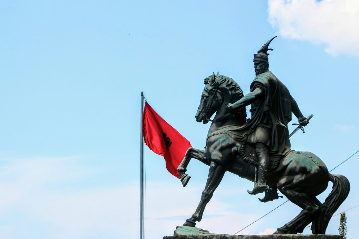 Bronze equestrian statue of a warrior on rearing horse with red Albanian flag against blue sky