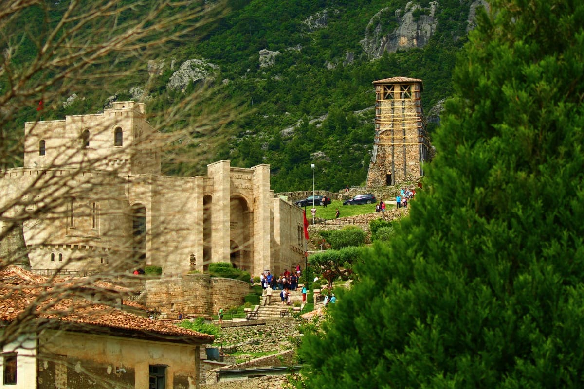 Ancient stone fortress with tower and visitors in mountainous Albanian landscape surrounded by green vegetation