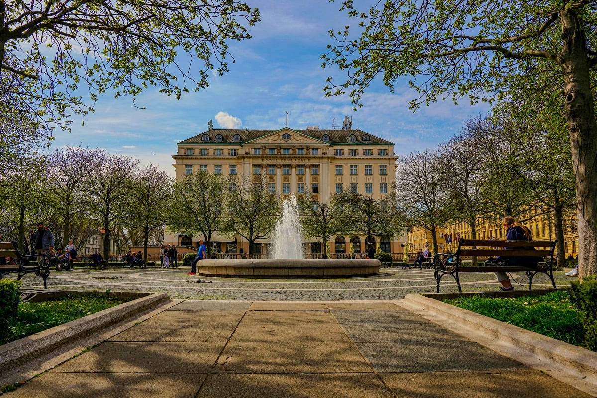 Neoclassical building with fountain in Zagreb city square surrounded by trees and visitors on benches