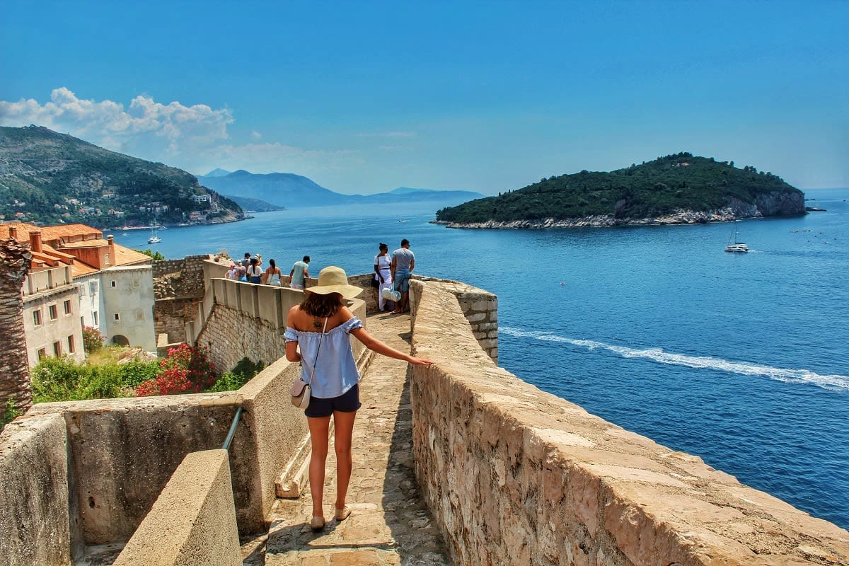 Tourist walking on ancient stone walls overlooking Adriatic Sea and island near Dubrovnik, Croatia
