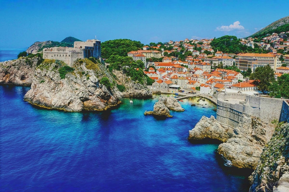 Coastal view of Dubrovnik's Old Town with fortress walls, red-roofed buildings, and turquoise Adriatic Sea surrounded by rock
