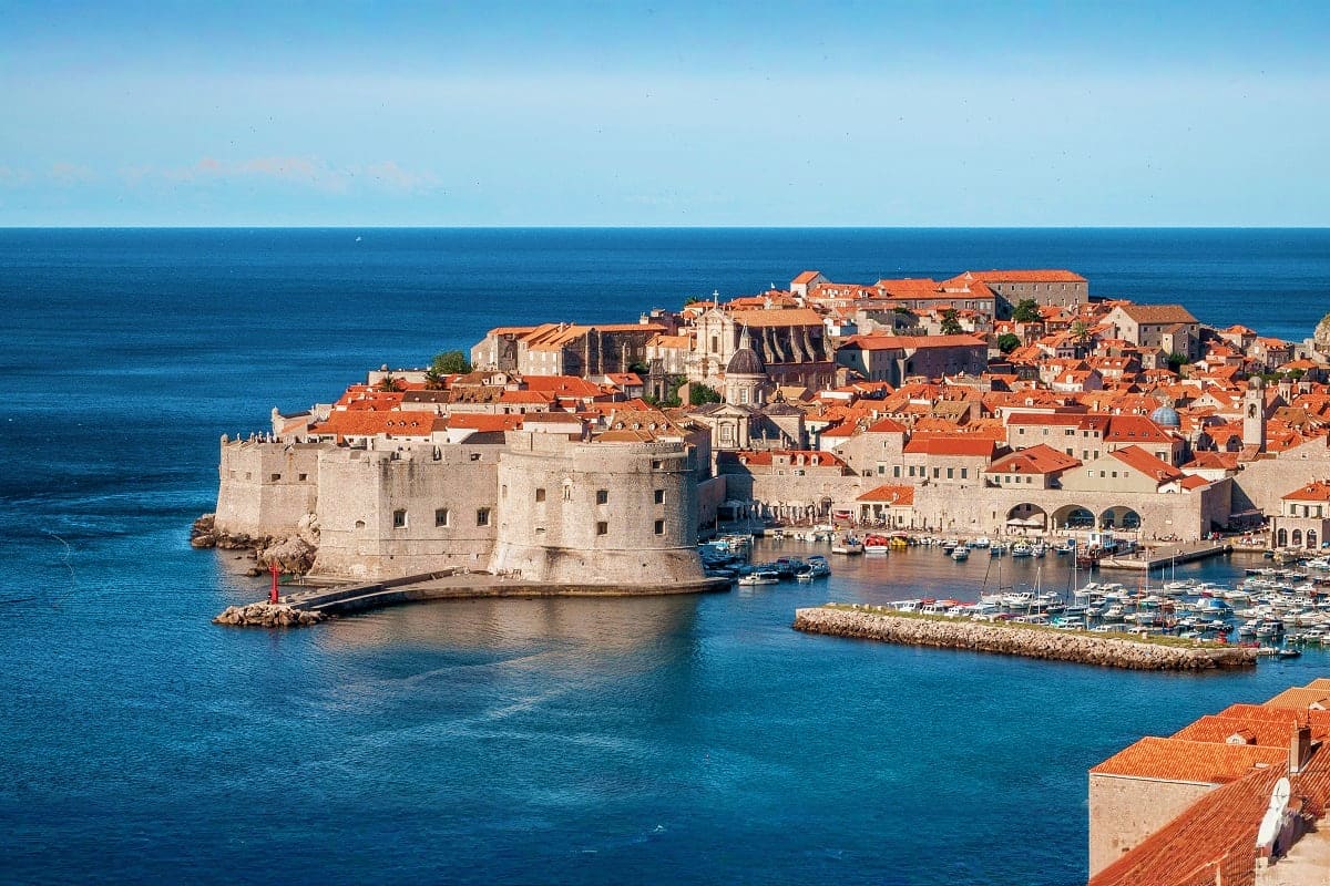 Aerial view of Dubrovnik's Old Town fortress walls and terracotta-roofed buildings overlooking the Adriatic Sea with moored b