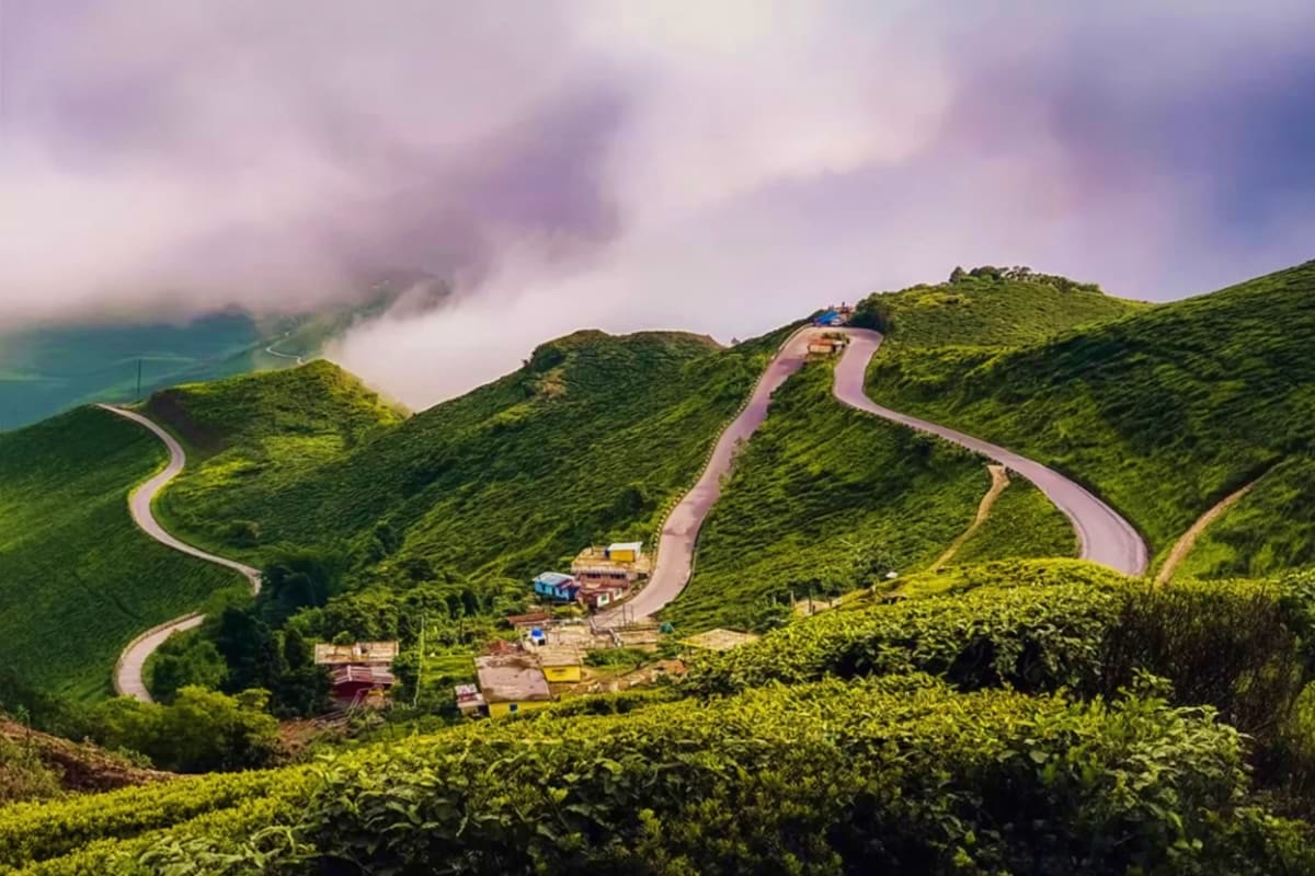 Winding mountain road through lush green hills with misty valleys and a scenic viewpoint structure visible on the hillside in