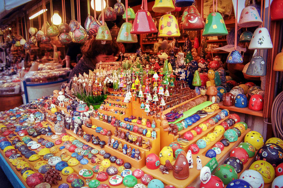 Colorful hand-painted wooden nesting dolls and decorative bells displayed on tiered shelves at a traditional market stall