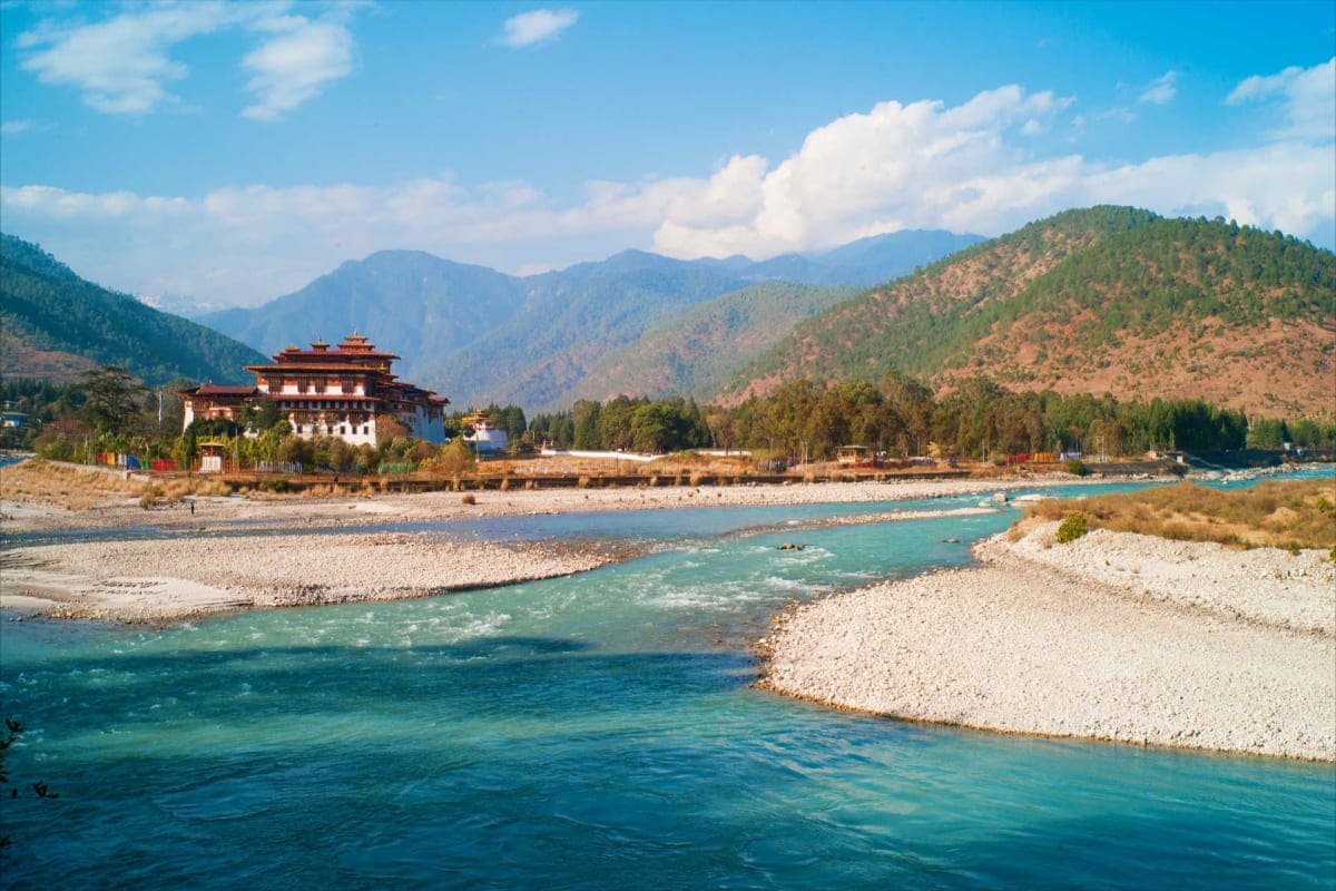 Punakha Dzong monastery beside turquoise river with forested mountains and blue sky in Bhutan