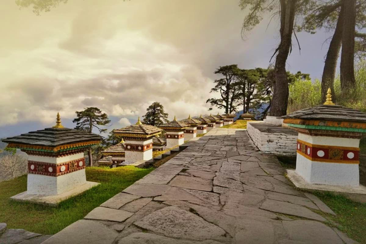 Stone pathway lined with ornate white and red prayer boxes with golden spires in traditional Bhutanese architecture nestled a
