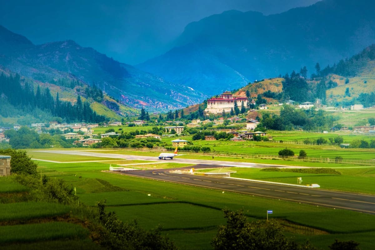 Paro International Airport runway with traditional Bhutanese monastery and Himalayan mountains in verdant valley landscape