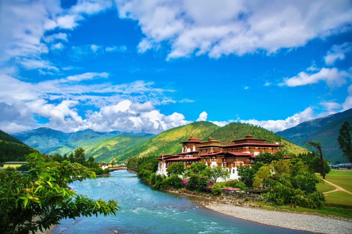 Punakha Dzong fortress beside turquoise river with green mountains and blue sky in Bhutan valley landscape