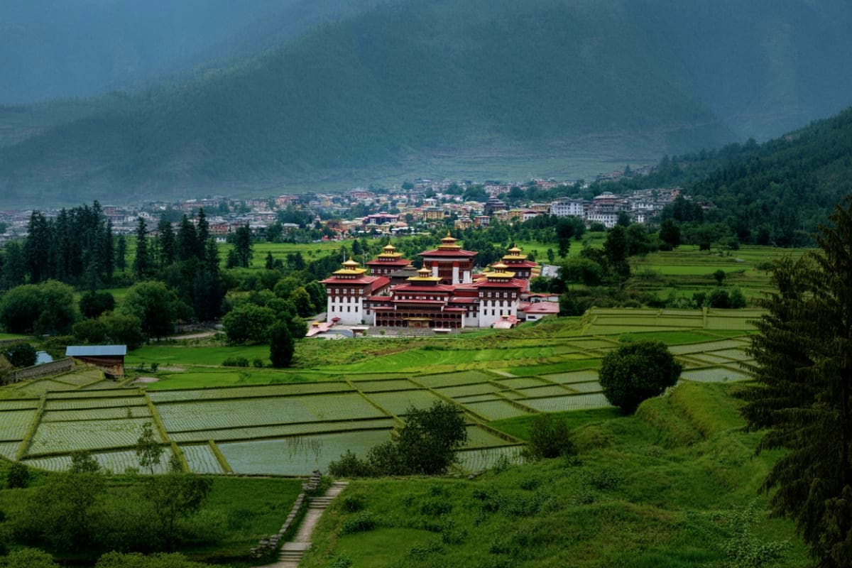 Drukgyel Dzong monastery with red and gold roofs surrounded by green rice terraces and forested mountains in Bhutan's Paro Va