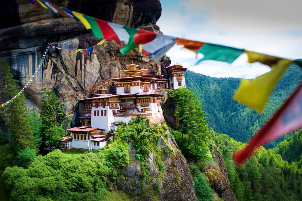 Tiger's Nest Monastery perched on a cliff edge surrounded by pine forests, with colorful prayer flags in the foreground, Bhut