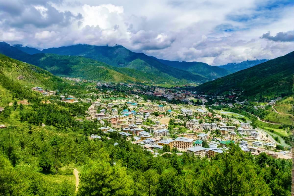 Aerial view of Thimphu valley surrounded by green forested mountains with modern buildings nestled in the landscape under clo