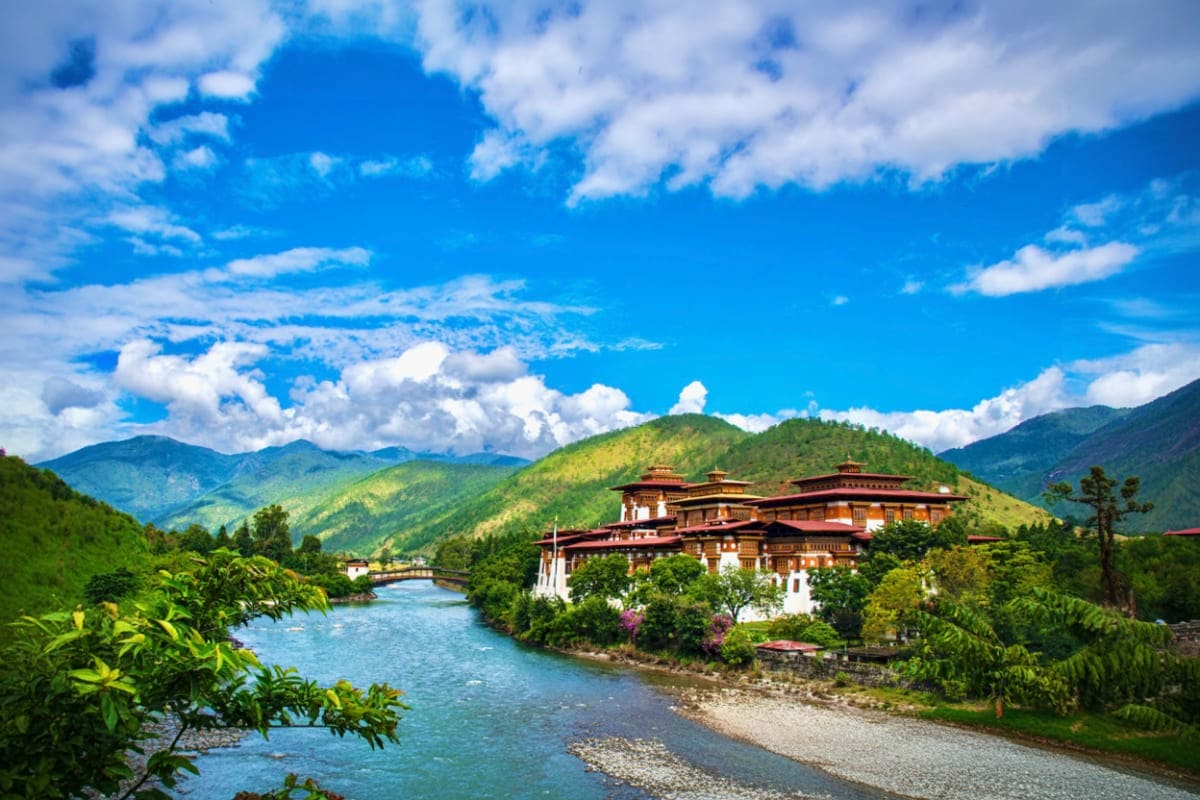 Punakha Dzong monastery with golden roofs beside turquoise river surrounded by green mountains under blue sky with white clou