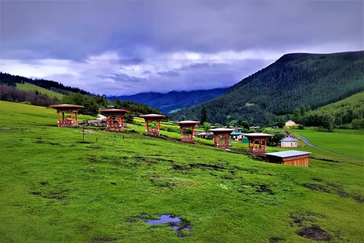 Traditional red Bhutanese prayer gates and buildings in lush green Haa Valley with forested mountains and cloudy sky