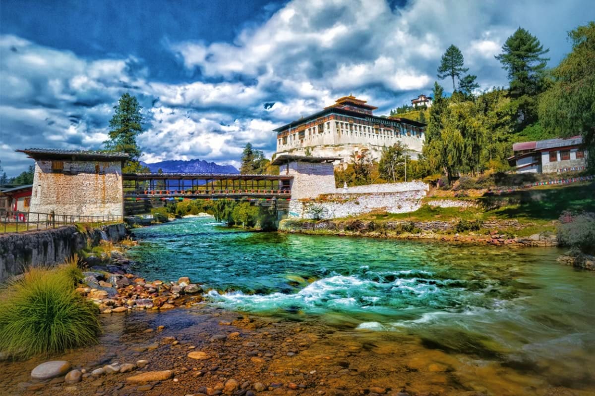 Rinpung Dzong fortress overlooking turquoise river with wooden bridge and pine trees in Bhutan's Paro Valley