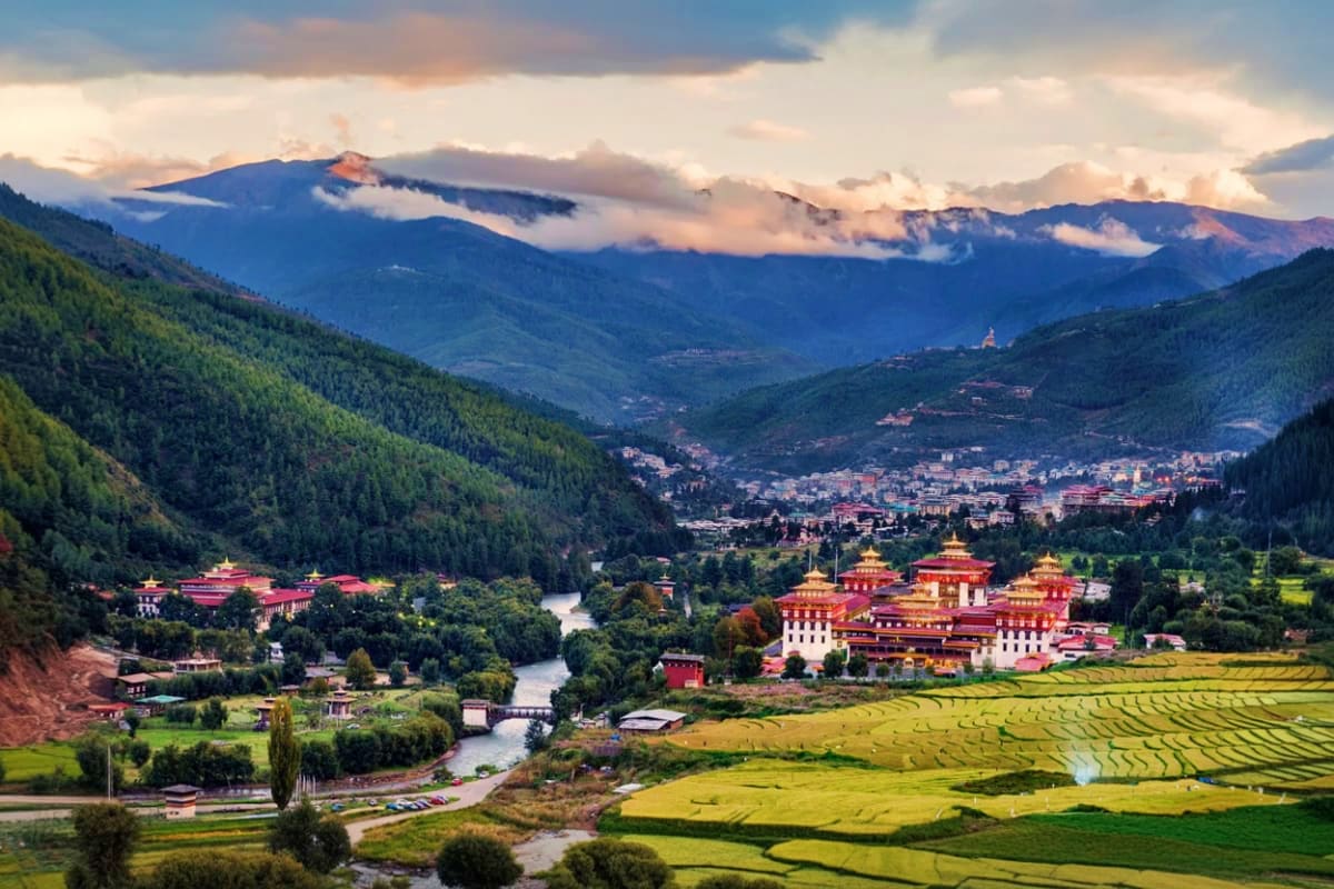 Punakha Dzong monastery with red and gold roofs overlooking river valley, terraced rice fields, forested mountains, and cloud