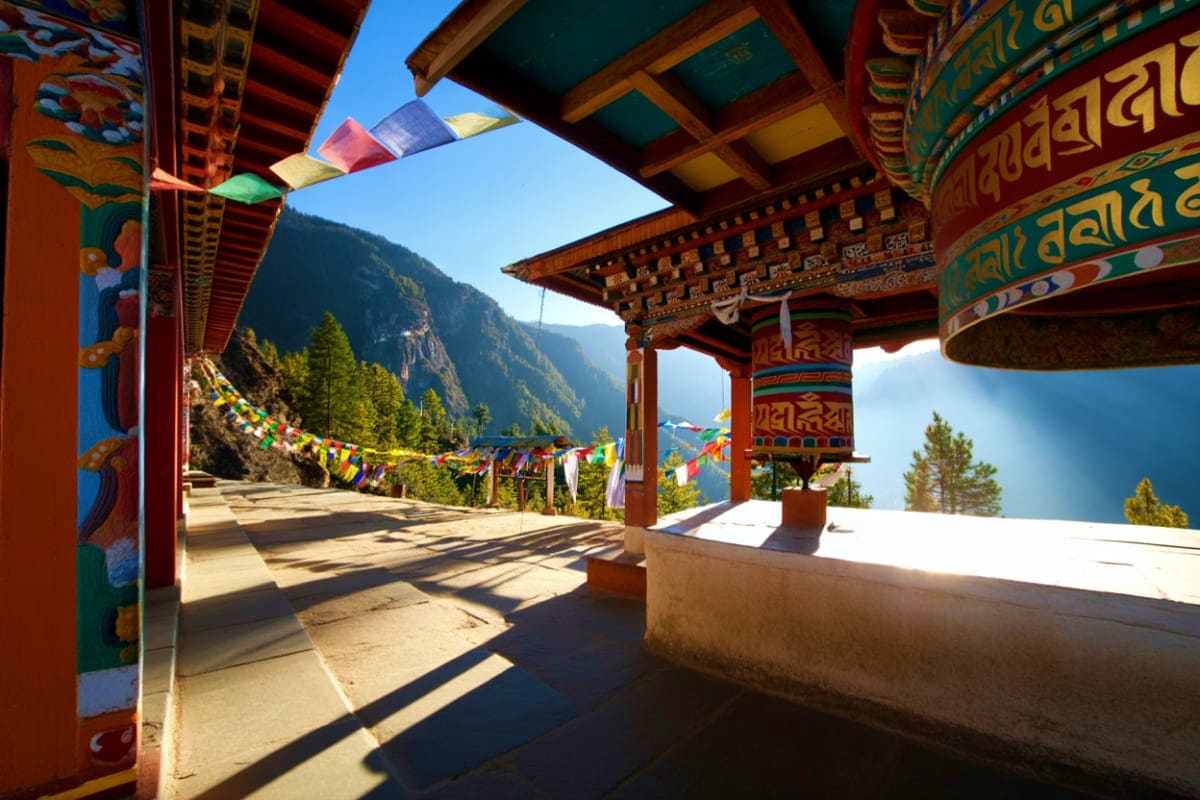Bhutanese monastery with colorful prayer flags overlooking forested mountain valley and clear blue sky