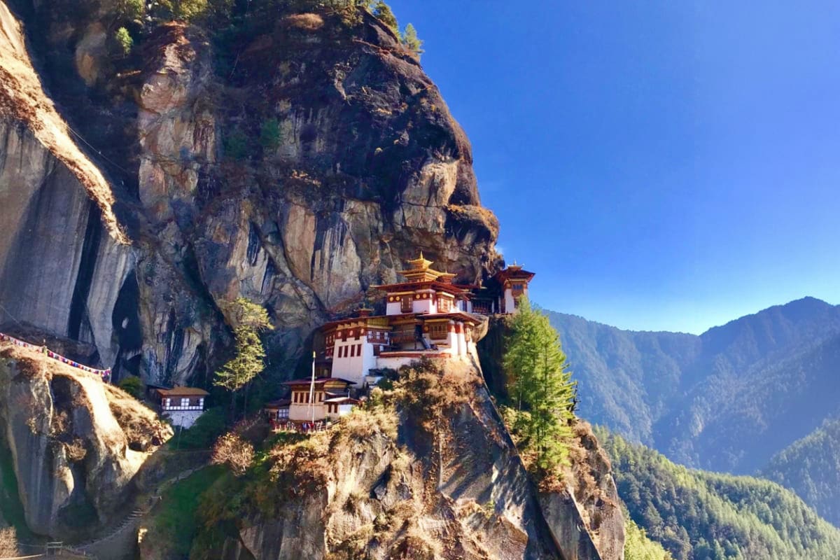 Tiger's Nest Monastery perched on a cliff overlooking a forested valley in Bhutan under clear blue sky