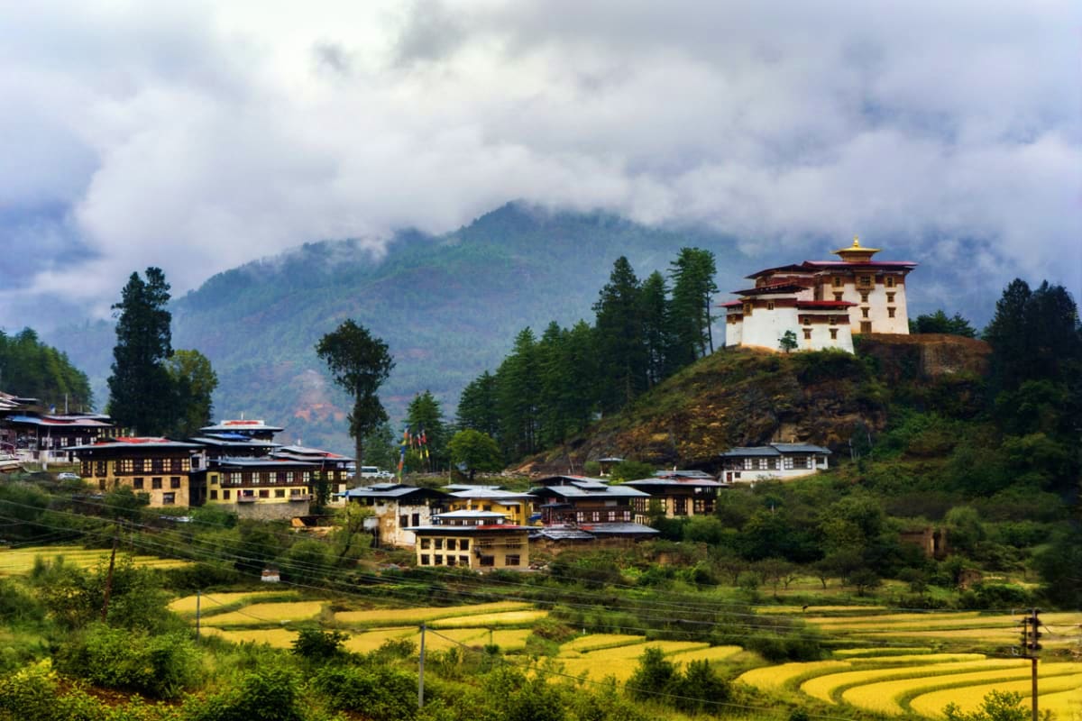Paro Taktsang (Tiger's Nest) monastery perched on a hillside overlooking a Bhutanese valley with traditional buildings and go