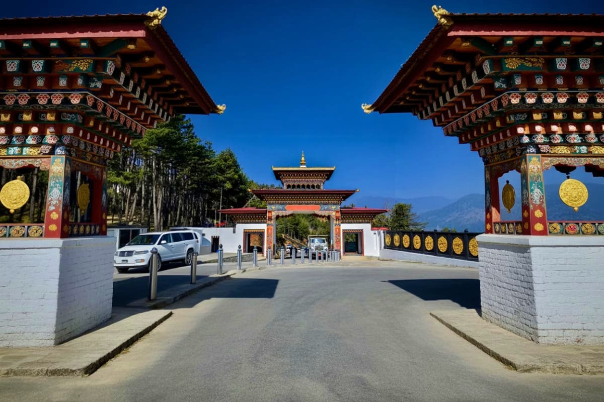 Bhutanese temple gateway with ornate red roofs, golden finials, and traditional decorative elements framing entrance to monas