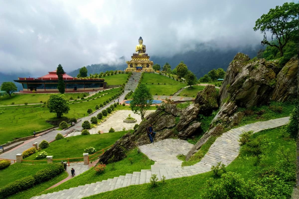 Golden Buddha statue on hilltop surrounded by green meadows, stone pathways, and mountain landscape in Bhutan