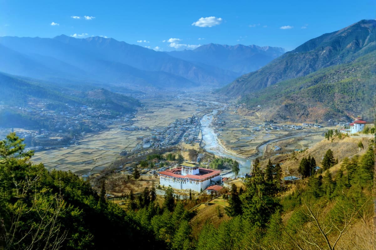 Aerial view of Paro Valley in Bhutan with Paro Dzong monastery, winding river, agricultural fields, forested mountains, and b