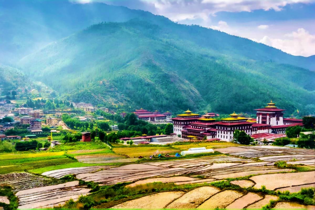 Tashichho Dzong fortress with golden roofs overlooking rice paddies and forested mountains in Thimphu, Bhutan