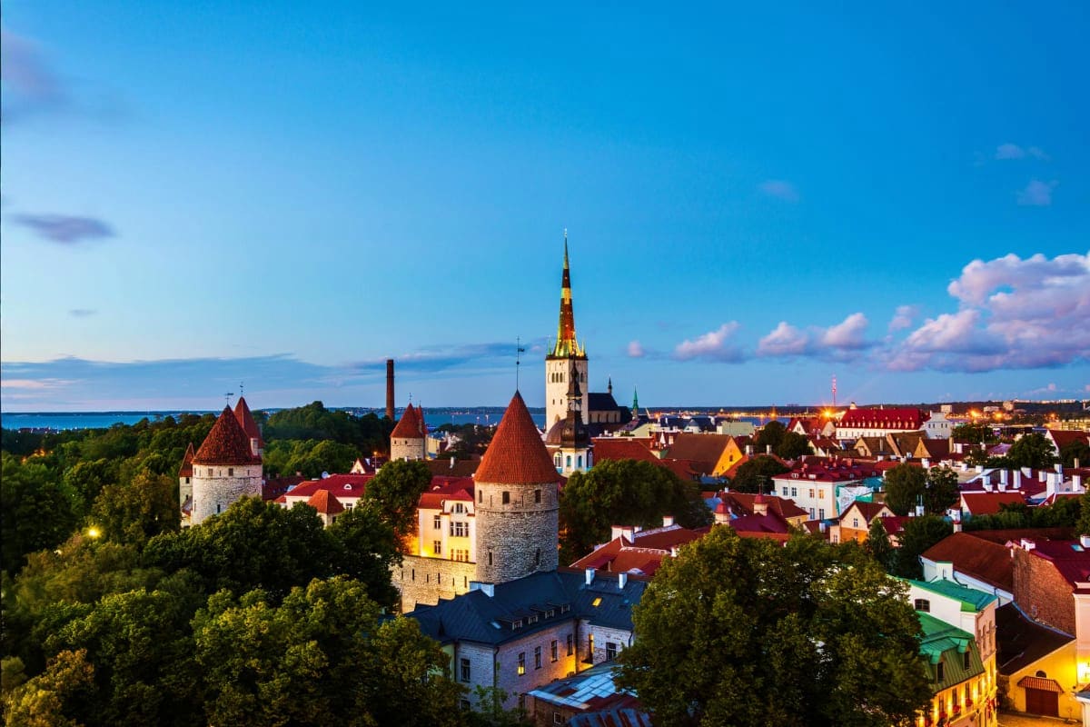 Aerial view of Tallinn Old Town with medieval towers, red-roofed houses, and church spires against blue sky and Baltic Sea co