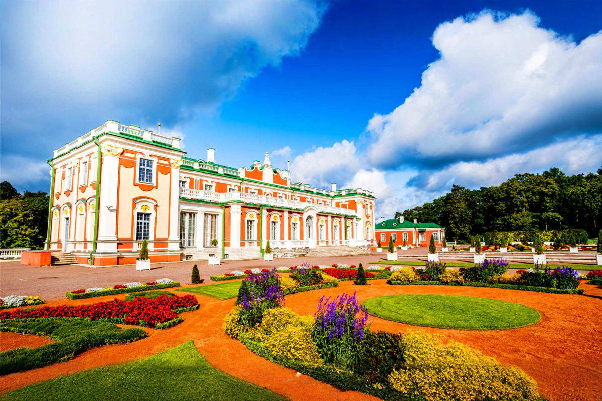 Orange and white Baroque palace with green trim and ornate gardens featuring colorful flower beds and manicured lawns under b