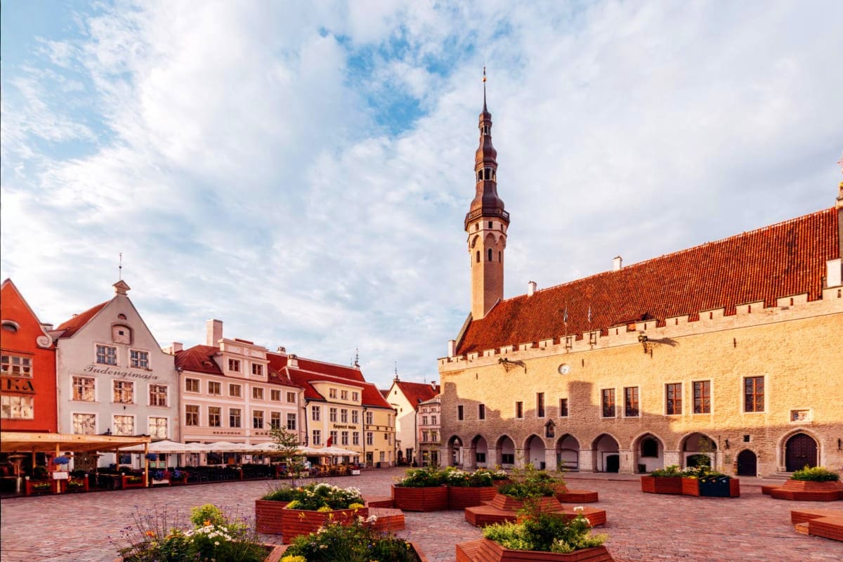 Tallinn Town Hall Square with medieval architecture, red-roofed buildings, and tall spire tower under cloudy sky