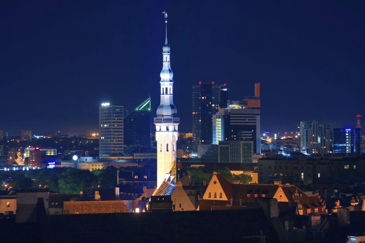 Illuminated Alexander Nevsky Cathedral dome rising above Tallinn's Old Town rooftops at night with modern city skyline