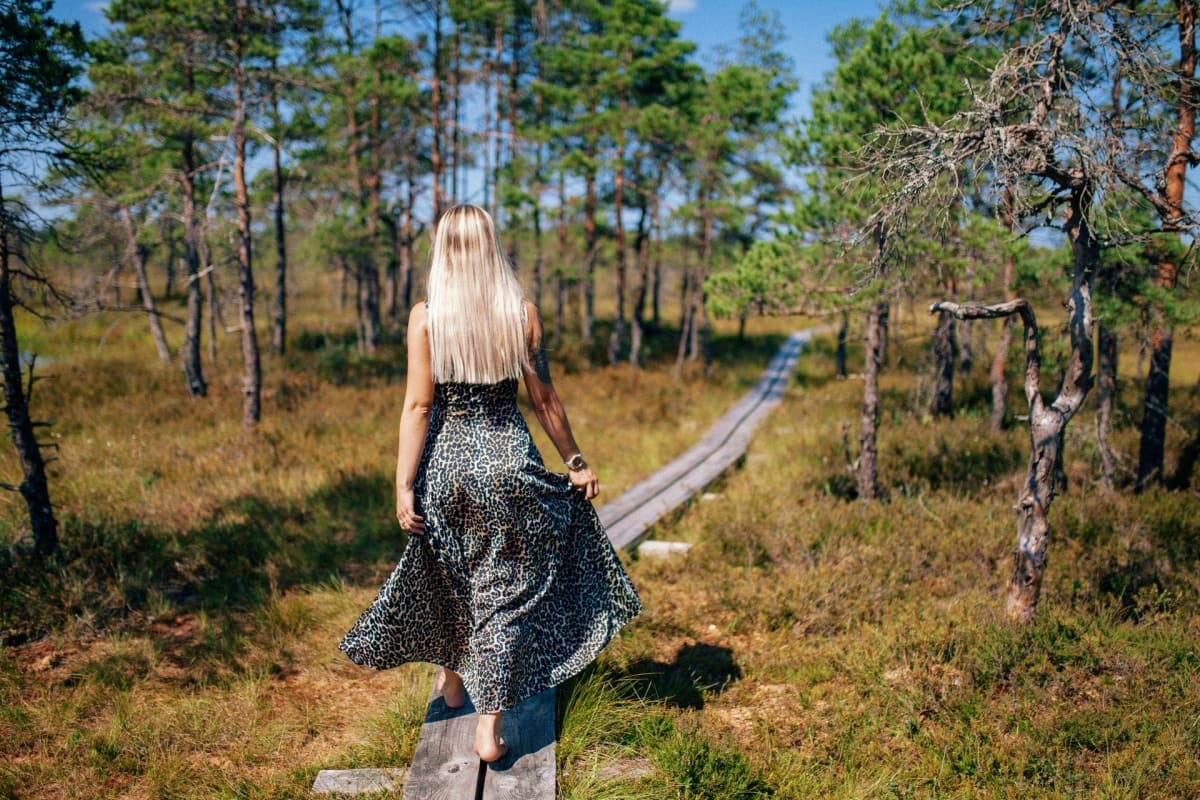 Woman with long blonde hair walking on wooden boardwalk through pine forest in Estonia