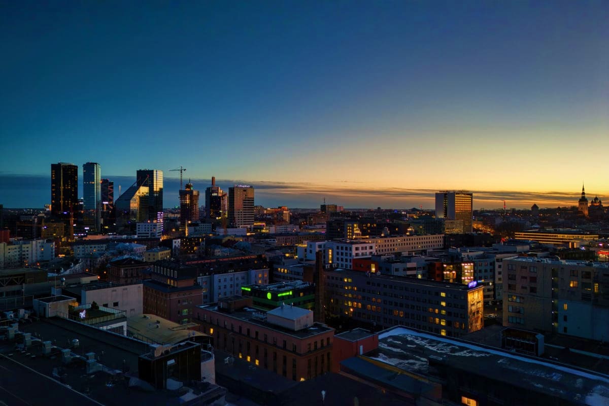 Urban skyline at dusk with illuminated office and residential buildings overlooking a body of water at sunset