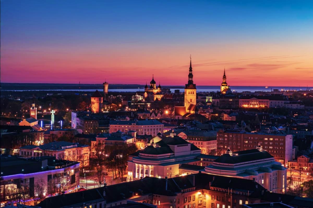 Tallinn Old Town skyline at sunset with illuminated churches and spires reflected in pink and orange twilight sky