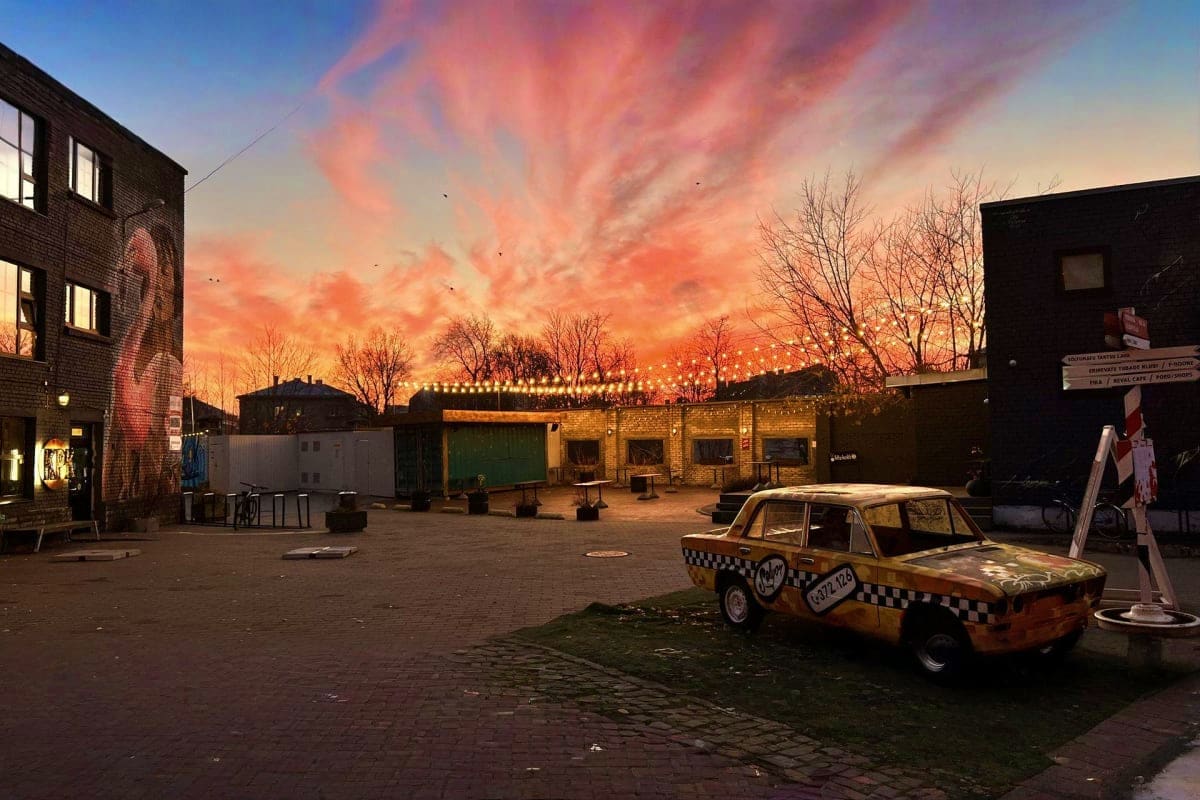 Vintage taxi car in an urban courtyard at sunset with brick buildings and festive string lights overhead in Tallinn