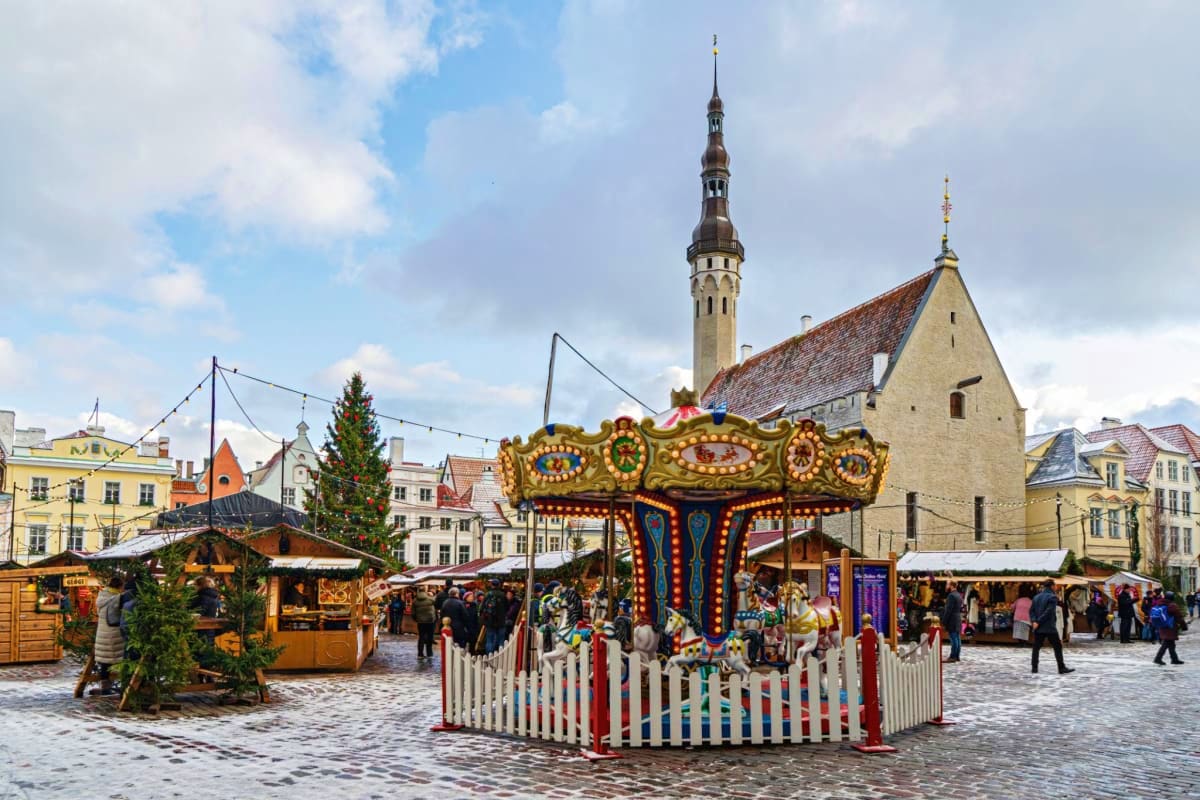 Traditional carousel with ornate decorations in Tallinn's Town Hall Square during Christmas market, historic church spire in 