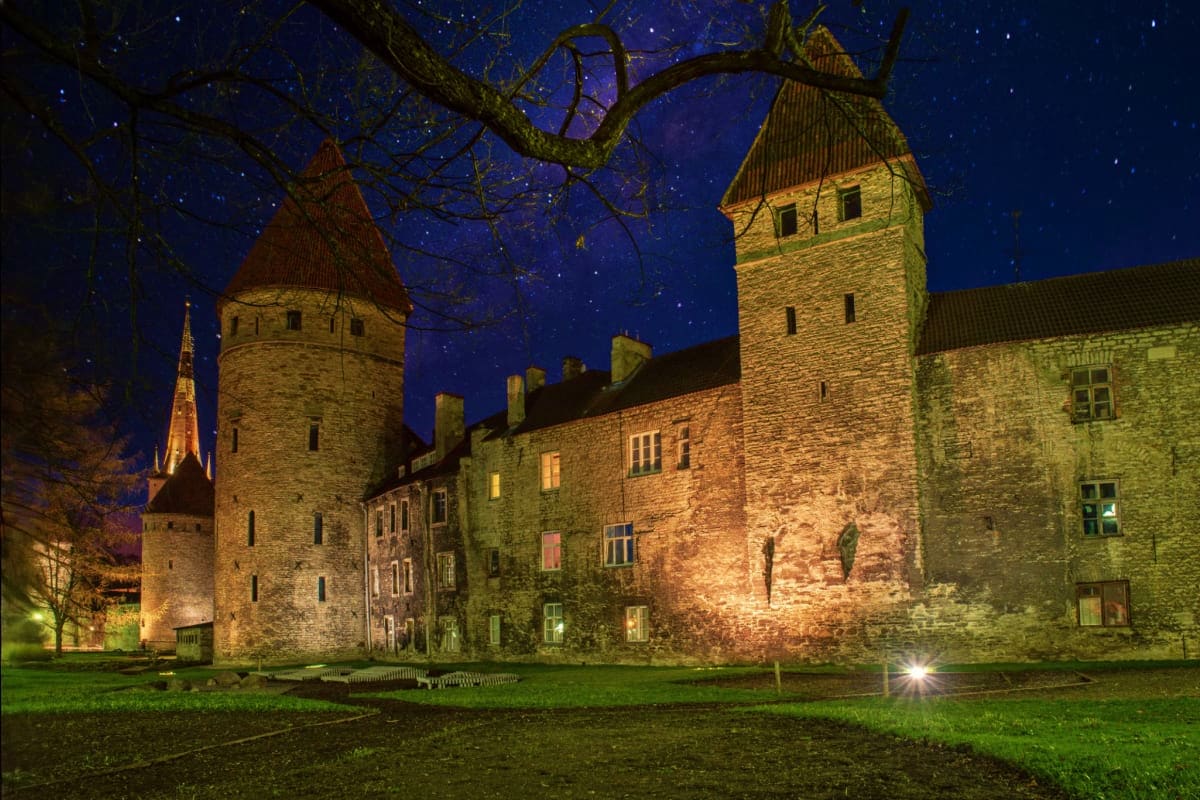Medieval Tallinn castle illuminated at night with stone towers, defensive walls, and starry sky overhead