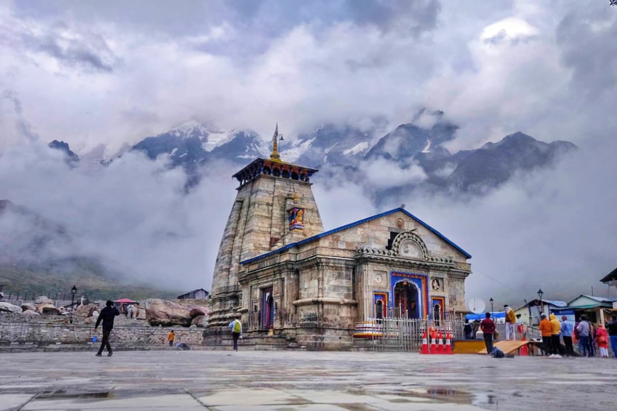 Ancient stone temple with golden spire in Himalayan valley surrounded by snow-capped mountains and clouds, pilgrims gathered 