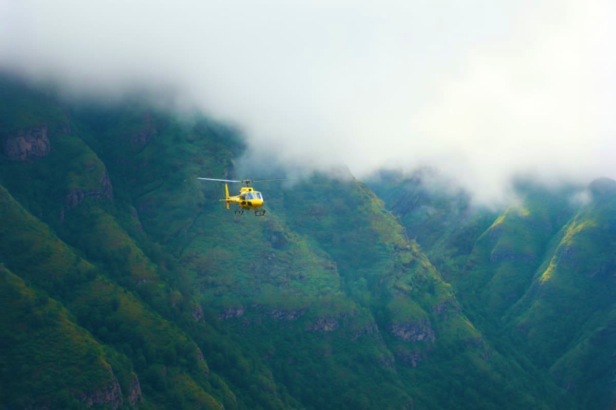 Yellow helicopter flying over misty green mountain valleys with steep forested cliffs during Dham Yatra journey