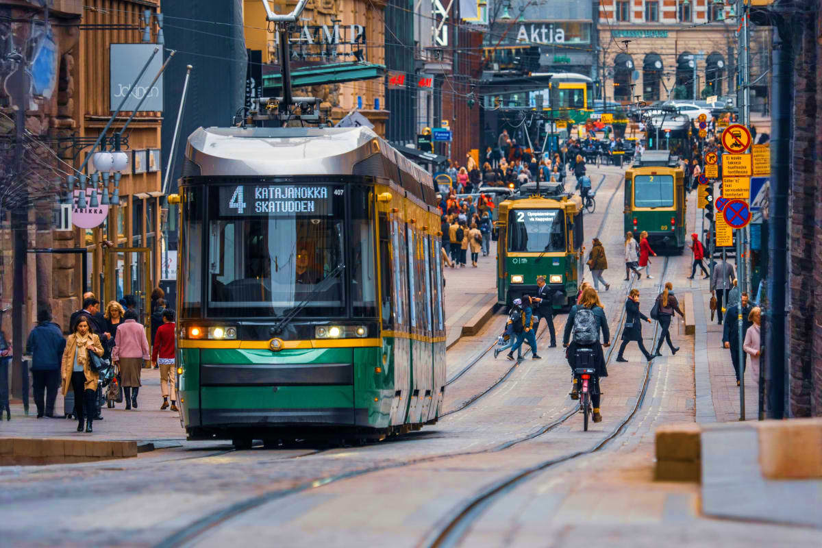 Green and white tram on tracks in Helsinki city street with pedestrians and cyclists, Aktia building visible in background